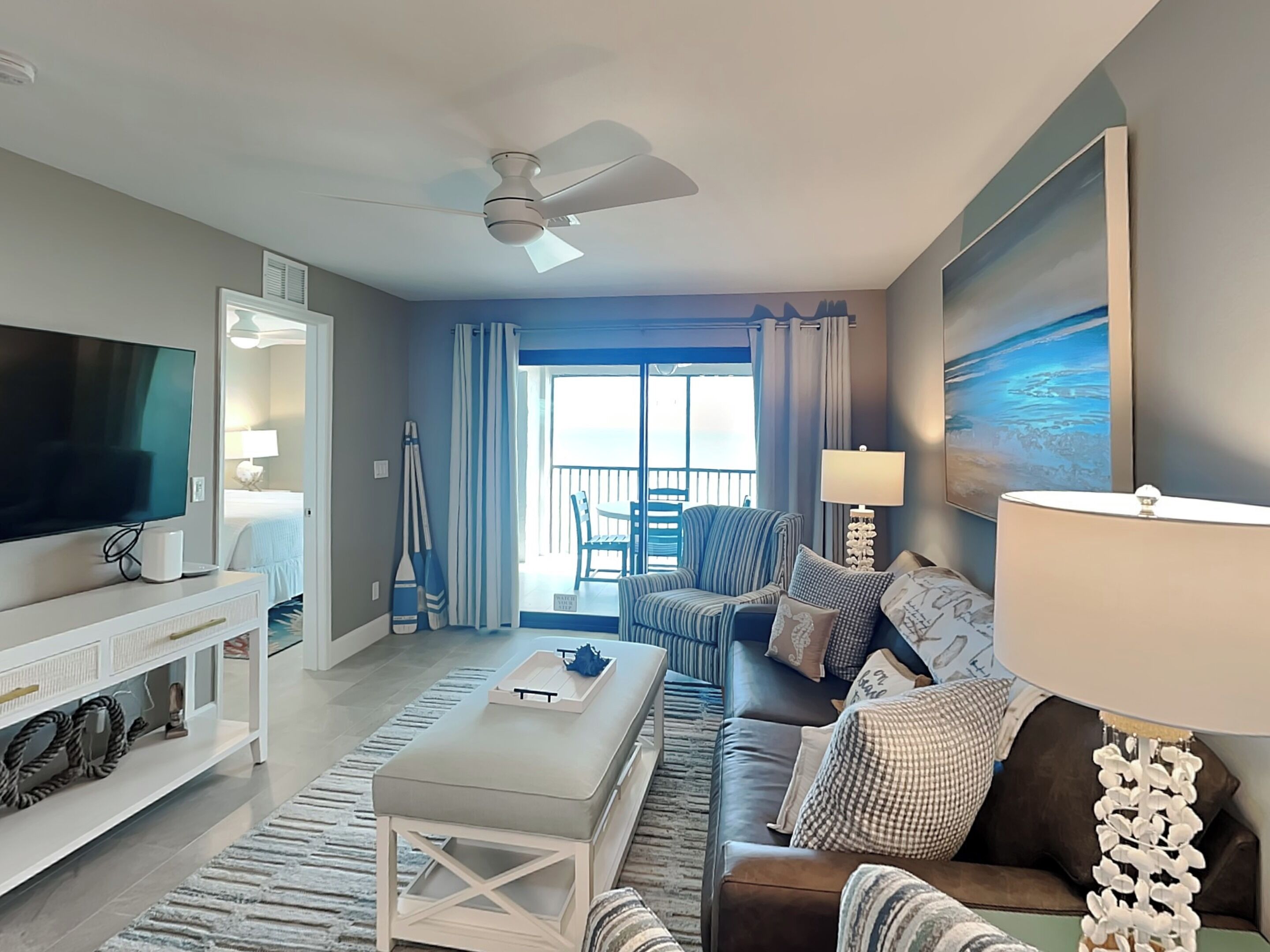 A modern living room with a flat-screen TV, a ceiling fan, a sofa, a coffee table, and a view of the balcony.