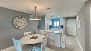 A modern kitchen with white cabinetry, a central island, and a dining area with a round table and chairs. - Seaside 508 | Updated Interior + Gulf Views (Fort Myers Beach)
