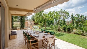 Eine Terrasse im Freien mit einem langen Esstisch, umgeben von Grünpflanzen und Blick auf die Landschaft.