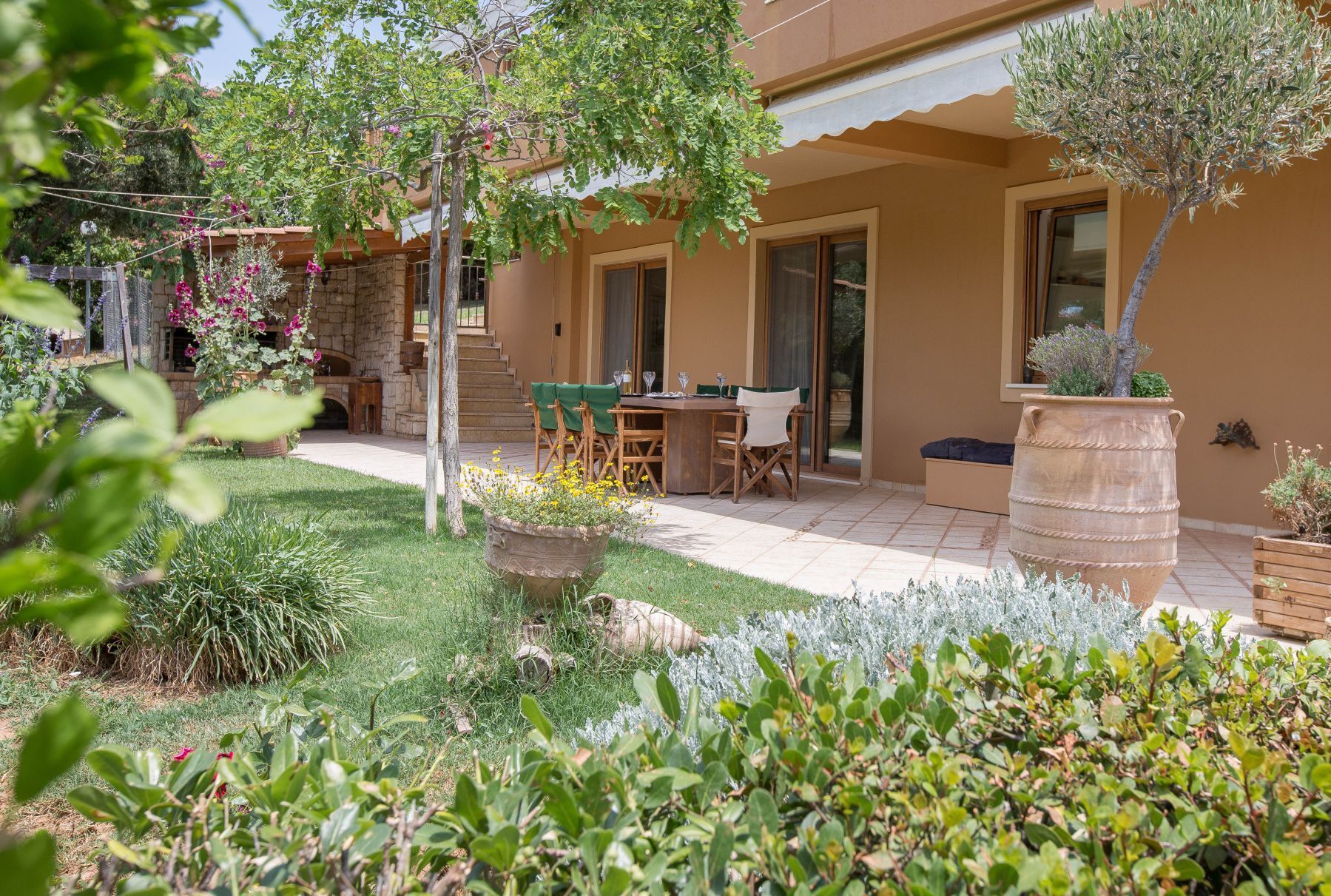 A patio with a table and chairs, surrounded by a garden with various plants and a stone wall.