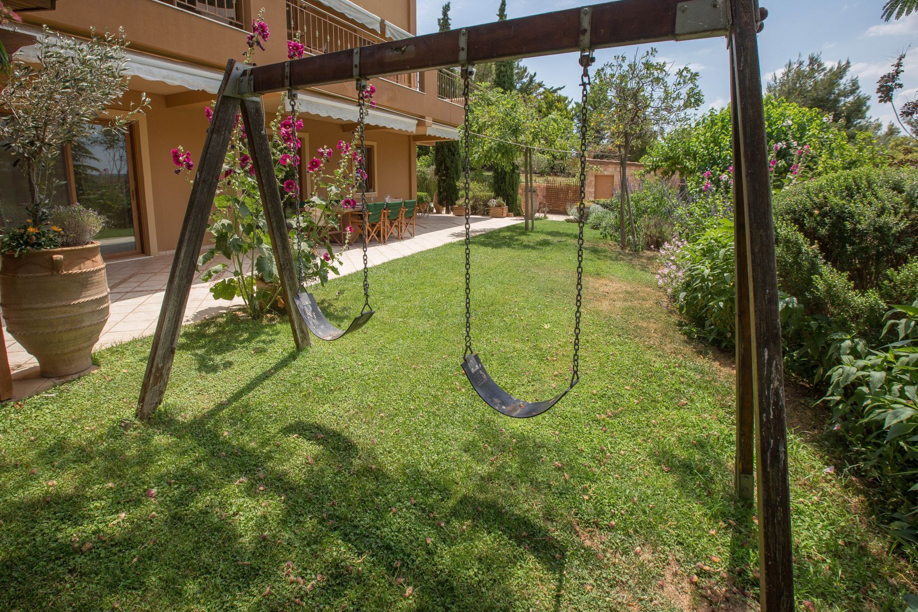 A wooden swing set in a well-maintained garden with a house in the background.