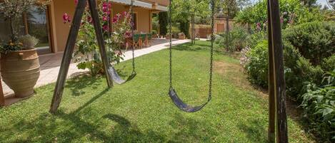 A wooden swing set in a well-maintained garden with a house in the background.