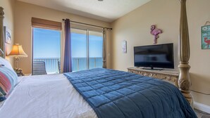 A bedroom with a large bed, a television, a balcony with a view, and a ceiling fan.
