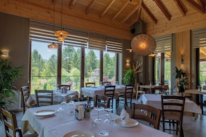 Un restaurante con varias mesas dispuestas para comer, amplias ventanas que ofrecen vistas al exterior y vigas de madera en el techo.