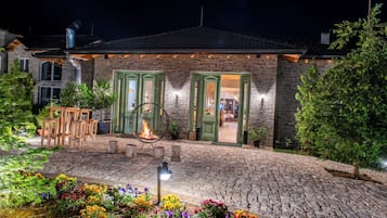 Un edificio de piedra con puertas verdes, una fogata, asientos al aire libre y un patio empedrado.