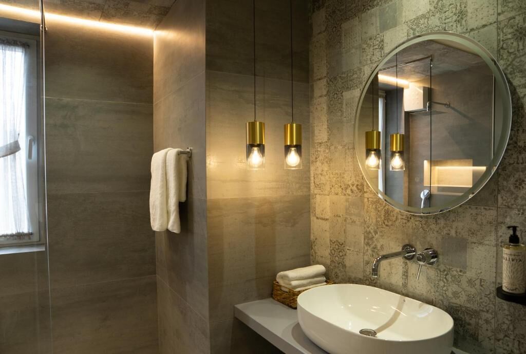 Ein modernes Badezimmer mit einem großen, ovalen Waschbecken, einem runden Spiegel und zwei Pendelleuchten.