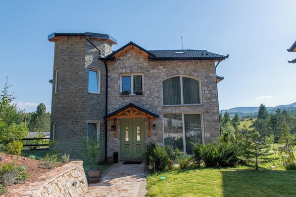 Une maison en pierre avec une porte verte, un petit porche et un chemin de pierre menant à l’entrée.