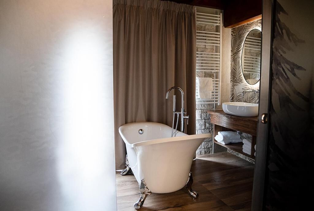 A bathroom with a freestanding bathtub, a wooden vanity with a sink, and a stone wall.