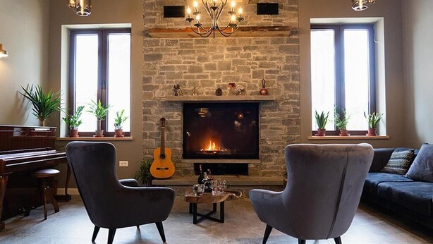 Un salon avec une cheminée, un piano, deux fauteuils, un canapé et une guitare.