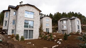 Une maison moderne en pierre, à deux étages, dotée d’une grande fenêtre à l’avant et d’un petit balcon.