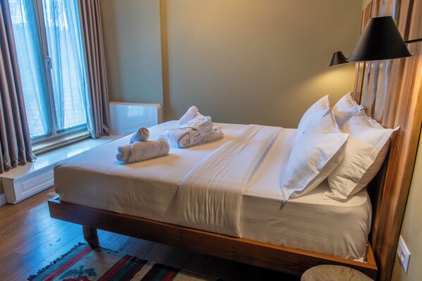 A neatly made bed with white linens and pillows, a bedside lamp, and a window with curtains. - Ura e Kovacit Agrotourism (Voskopojë)