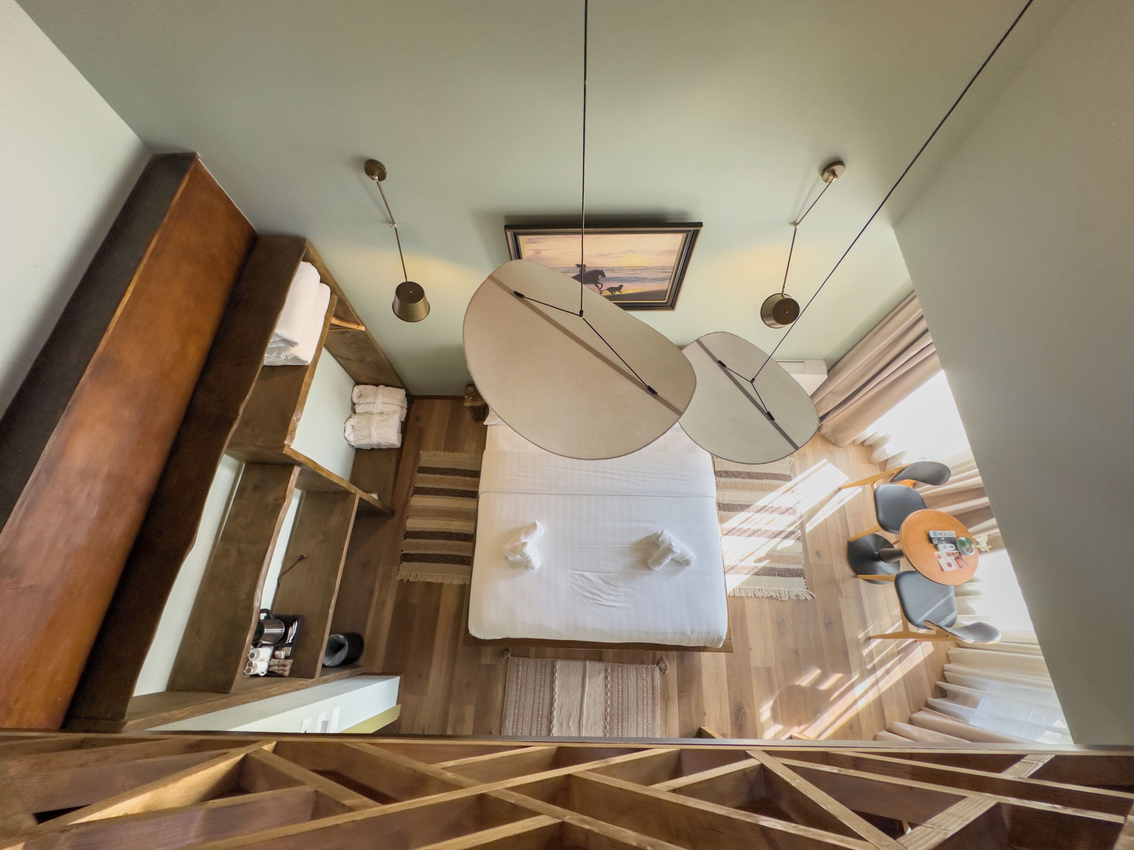 A modern hotel room with a wooden staircase, a large bed, and a ceiling-mounted light fixture.