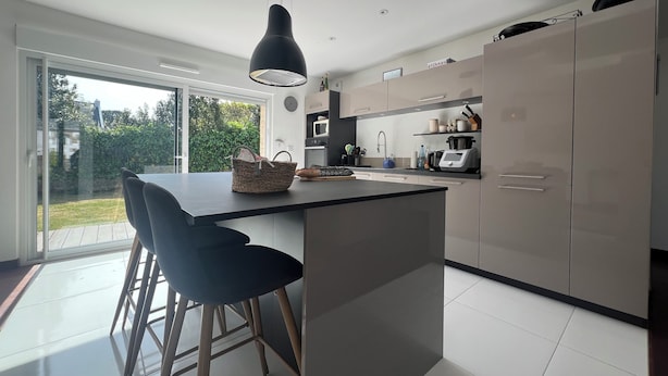 Una cocina moderna con una isla central, taburetes de bar y vistas al jardín a través de amplios ventanales.