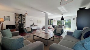 Una sala de estar moderna con sofás, una mesa de centro e iluminación colgante. Hay una zona de comedor con sillas y una mesa, y una cocina con estufa.