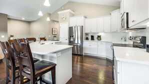 A modern kitchen with white cabinetry, stainless steel appliances, and a central island with seating. - Fairway Lake Retreat (Camdenton)