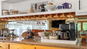 A kitchen with wooden cabinets, a coffee maker, and a glass display case. - Lakefront Daze – Stay for 6 w/ Pool Table & Outdoor Oasis (New Braunfels)