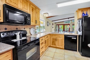 A kitchen with wooden cabinets, a black microwave, a stove, and a refrigerator. - Lakefront Daze – Stay for 6 w/ Pool Table & Outdoor Oasis (New Braunfels)