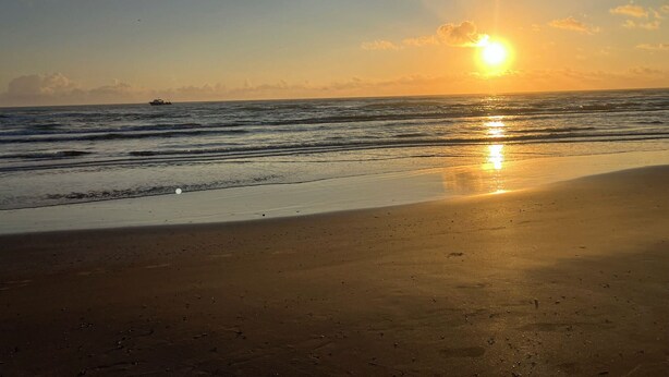A beach with a sunset over the ocean, a boat in the distance, and a clear sky. - Beach view w/ large balcony 200' from sand. Heated pool, hot tub, 4 beds, 2 bath (South Padre Island)