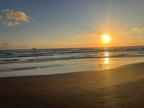 A beach with a sunset over the ocean, a boat in the distance, and a clear sky.