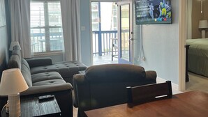 A living room with a sofa, a dining table, a TV mounted on the wall, and a ceiling fan. - Beach view w/ large balcony 200' from sand. Heated pool, hot tub, 4 beds, 2 bath (South Padre Island)