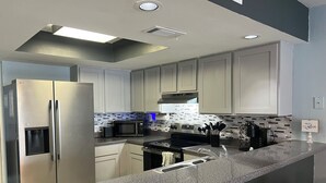 A modern kitchen with stainless steel appliances, a granite countertop, and a backsplash with a mosaic tile pattern. - Beach view w/ large balcony 200' from sand. Heated pool, hot tub, 4 beds, 2 bath (South Padre Island)
