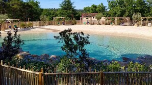 A clear pool surrounded by a wooden fence, with a small building and trees in the background.