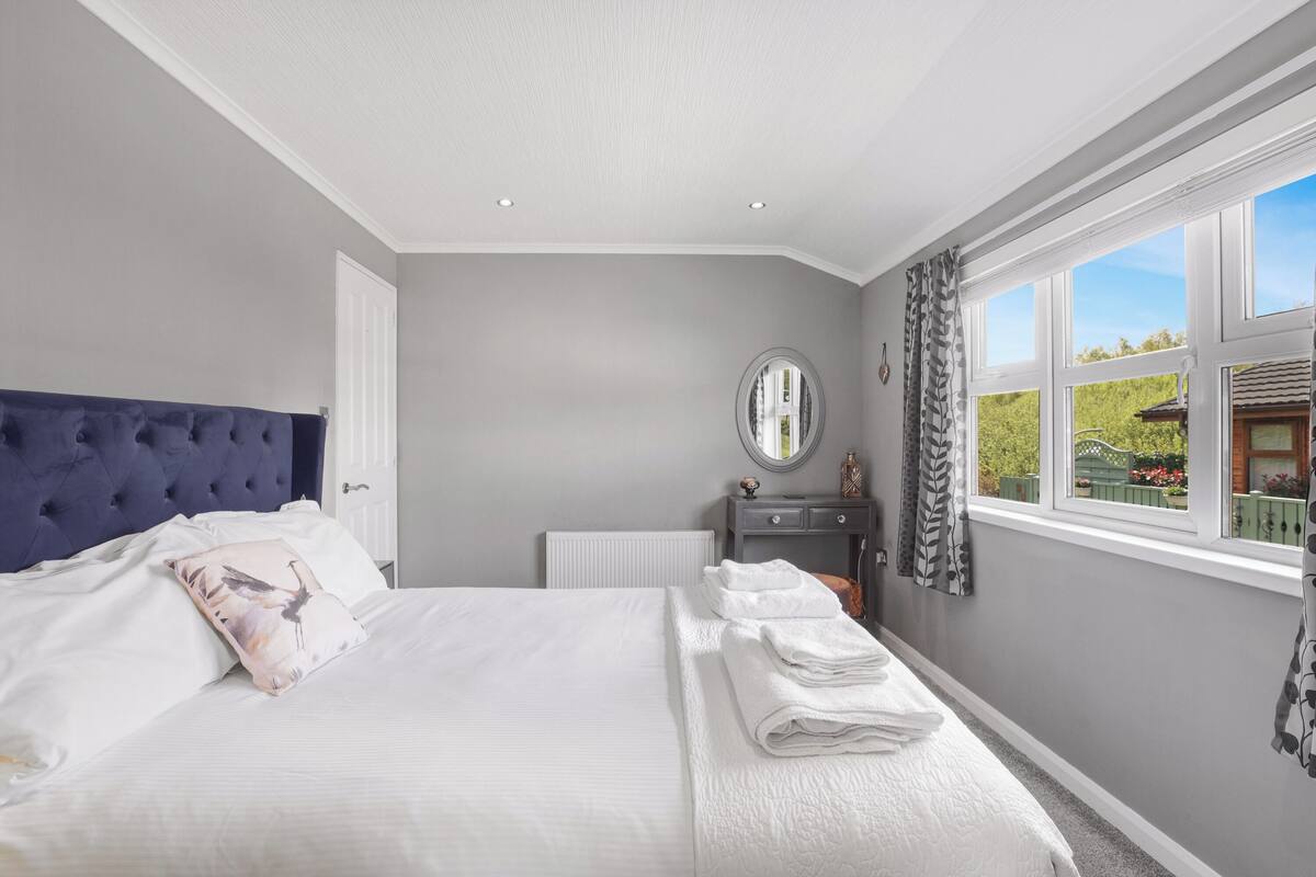 A bedroom with a large bed, a dresser, a mirror, and a window with a view of greenery.