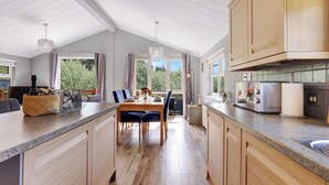A modern kitchen with wooden cabinets, a granite countertop, and a dining area with a table and chairs. - Fairway View - North East Escapes (Swarland)
