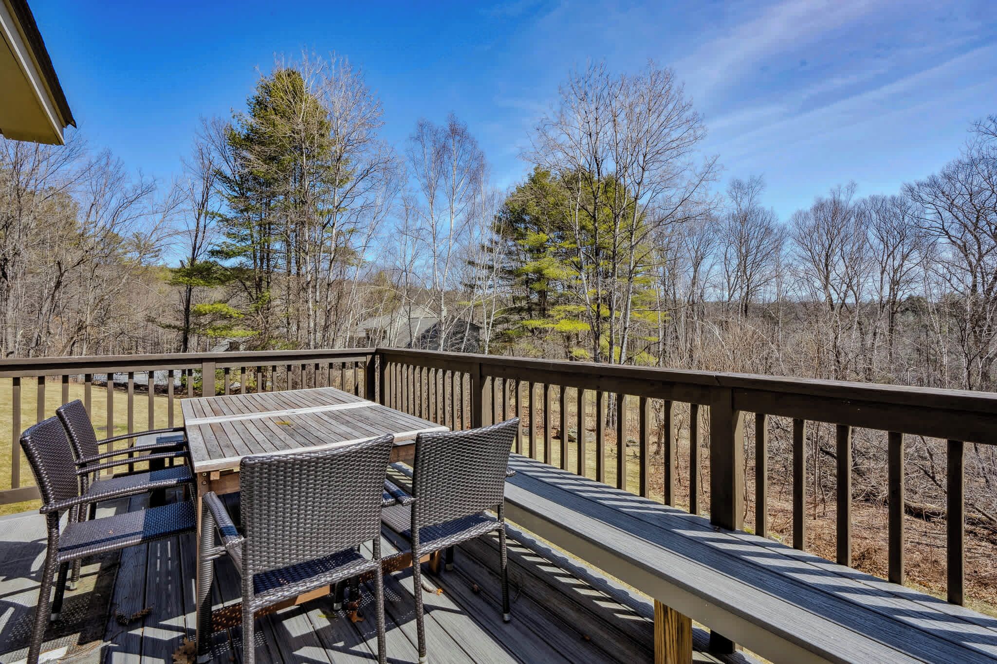 A wooden deck with a table and chairs, overlooking a forested area.