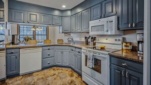 A modern kitchen with grey cabinets, a granite countertop, a built-in oven, a microwave, and a coffee maker. - Game Room Condo, Sugar Hill, Pet-Friendly (Quechee)