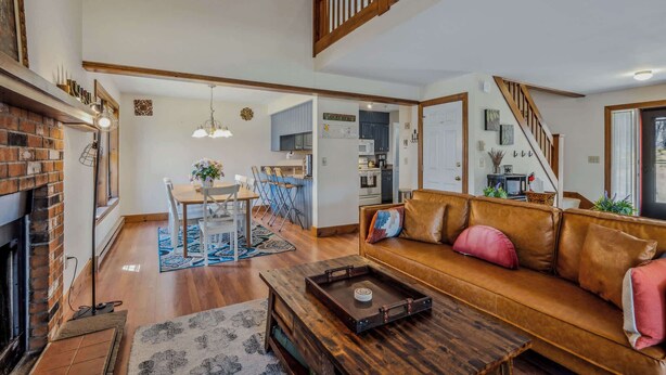 A spacious living room with a fireplace, a wooden coffee table, a leather sofa, and a dining area with a table and chairs. - Game Room Condo, Sugar Hill, Pet-Friendly (Quechee)