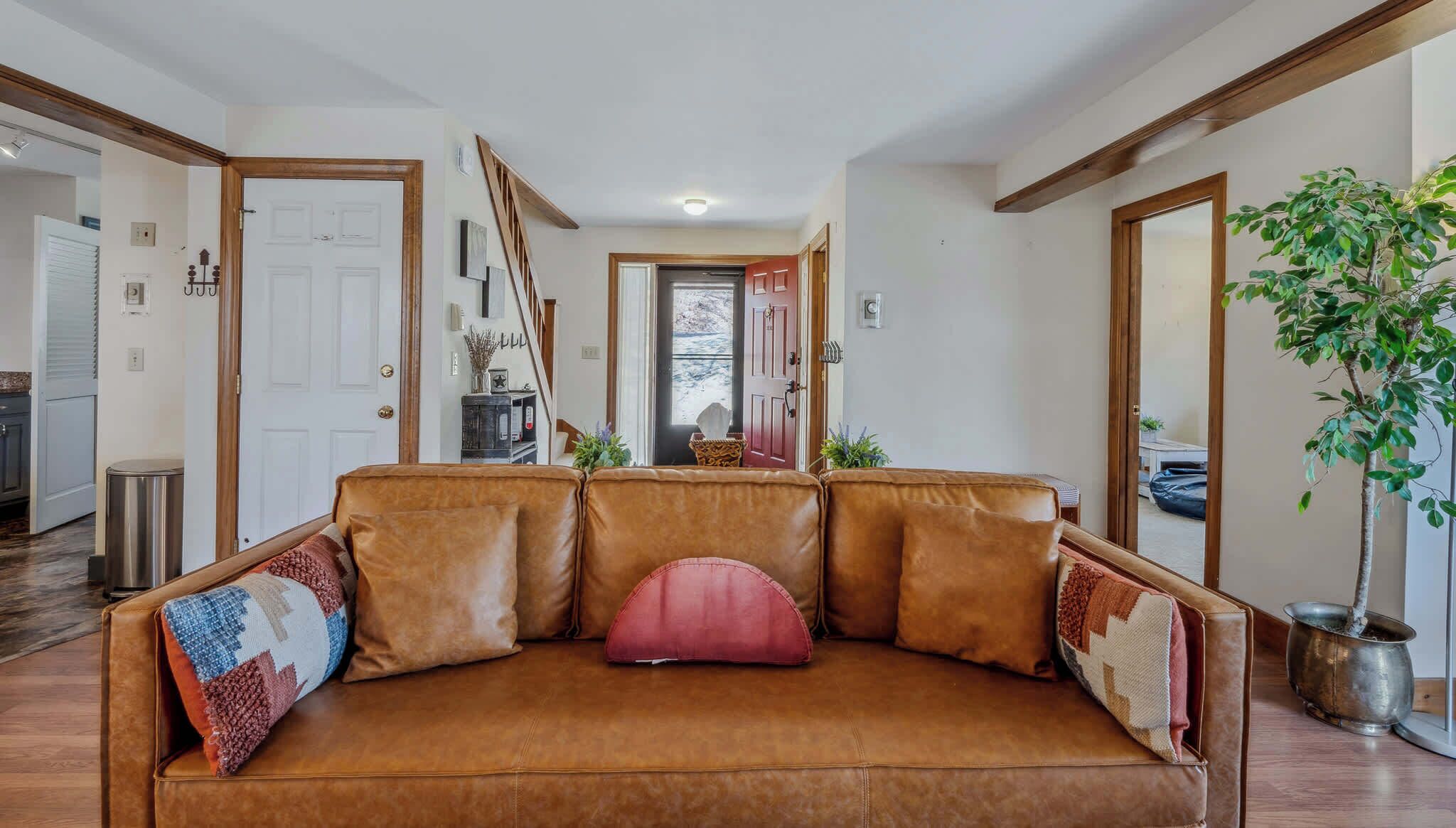 Ein braunes Ledersofa mit bunten Kissen in einer Diele mit Holzbalken und einem Blumentopf.