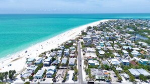 An aerial view of a coastal residential area with a beach, houses, and a road.