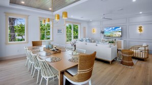 A spacious living room with a wooden ceiling, a white sofa, a dining table with chairs, and a crib.