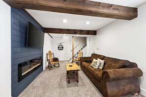 Una sala de estar acogedora con chimenea, un sofá de cuero marrón, un sillón mecedor de madera y una mesa de centro.