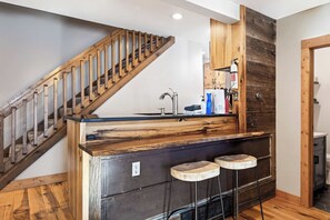 Una cocina con escalera de madera, un lavamanos y dos taburetes.