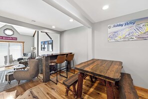 Un interior moderno con una mesa de comedor de madera, taburetes de bar y un cartel grande en la pared.