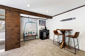 A room with a wooden bench, a small table with two chairs, a wall-mounted sign, and a ski-themed wallpaper. - Updated townhome - Walk to Holiday Valley (Ellicottville)
