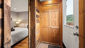 Ein Schlafzimmer mit Bett, Holzschrank und Fenster mit Blick auf Grünfläche.