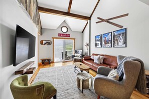A living room with a large flat-screen TV, a brown leather sofa, a green armchair, and a wooden coffee table.