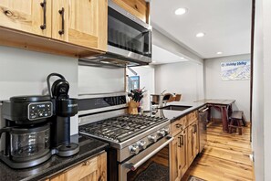 A modern kitchen with wooden cabinets, a stainless steel stove, a coffee maker, and a microwave. - Updated townhome - Walk to Holiday Valley (Ellicottville)