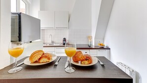 Una cocina moderna con armarios blancos, una mesa de comedor con cruasanes y jugo de naranja, y vista a la ciudad a través de una ventana.
