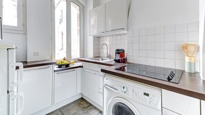 Cocina compacta con armarios blancos, lavavajillas integrado y ventana que proporciona luz natural.