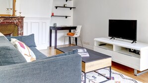 Una sala de estar moderna con un sofá gris, un televisor sobre un mueble blanco, una alfombra estampada y una araña.