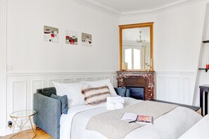 Une chambre à coucher bien rangée, avec un lit, une table de chevet, un miroir et des œuvres d’art accrochées au mur.
