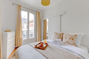 Une chambre d’hôtel avec un lit, un plateau avec des croissants et du jus d’orange, et une vue sur les bâtiments par la fenêtre.