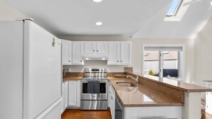 A modern kitchen with white cabinets, stainless steel appliances, and a granite countertop. - The Gathering Place - For 6 with Fire Pit (Mashpee)