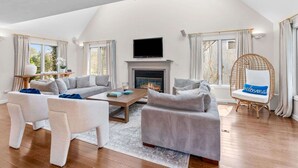 A spacious living room with a fireplace, a television mounted above it, and a comfortable seating area with sofas and a coffee table. - The Gathering Place - For 6 with Fire Pit (Mashpee)