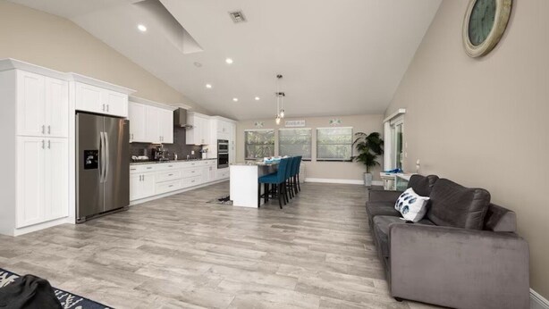 A spacious kitchen with white cabinets, a stainless steel refrigerator, and a dining area with blue chairs.