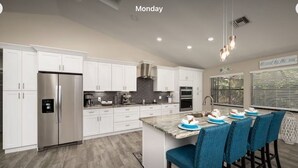 A modern kitchen with white cabinets, a stainless steel refrigerator, and a breakfast bar with blue chairs.
